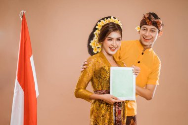balinese young couple showing tablet screen to camera. man and woman asian wearing kebaya and traditional cloth from bali