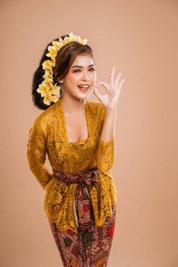 happy young balinese woman showing thumb up gesture to camera over isolated background
