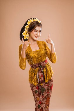 happy young balinese woman showing thumb up gesture to camera over isolated background