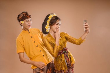 suprised balinese couple with kebaya while looking at her mobil phone screen over isolated background