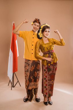 excited balinese couple put hands up looking at camera over brown background
