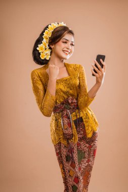 suprised balinese woman with kebaya while looking at her mobil phone screen over isolated background