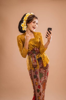 suprised balinese woman with kebaya while looking at her mobil phone screen over isolated background
