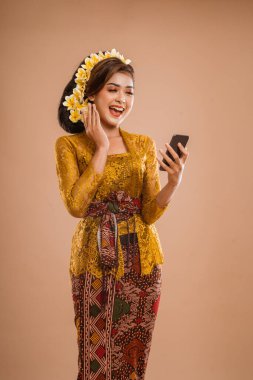 suprised balinese woman with kebaya while looking at her mobil phone screen over isolated background