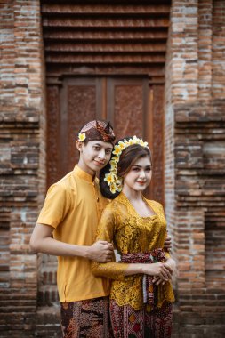 balinese couple portrait wearing kebaya dress standing in front of traditional bali gate