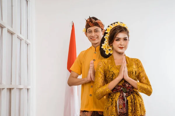 balinese couple with greeting gesture to camera. woman and man wearing traditional balinese costume over isolated background