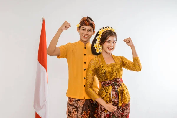 excited balinese couple put hands up looking at camera over brown background
