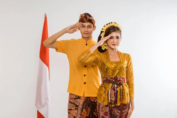 balinese couple salute to camera with indonesian flag in the background isolated over white background
