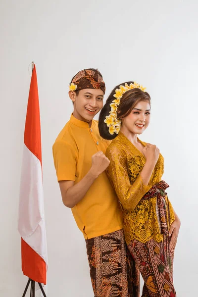 excited balinese couple put hands up looking at camera over brown background