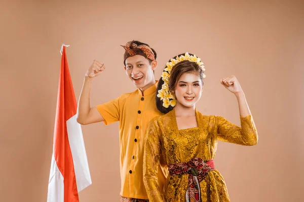 excited balinese couple put hands up looking at camera over brown background