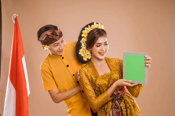 balinese young couple showing tablet screen to camera. man and woman asian wearing kebaya and traditional cloth from bali