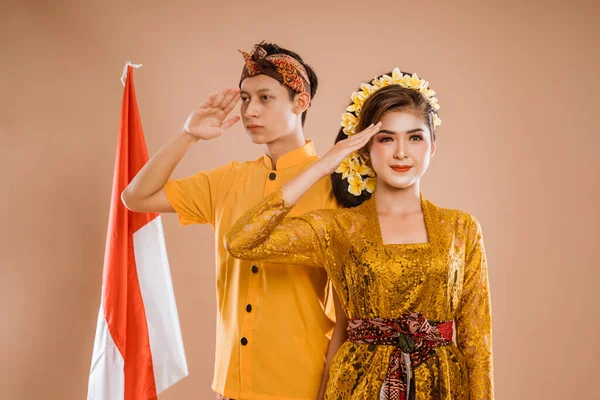 balinese couple salute to camera with indonesian flag in the background isolated over brown