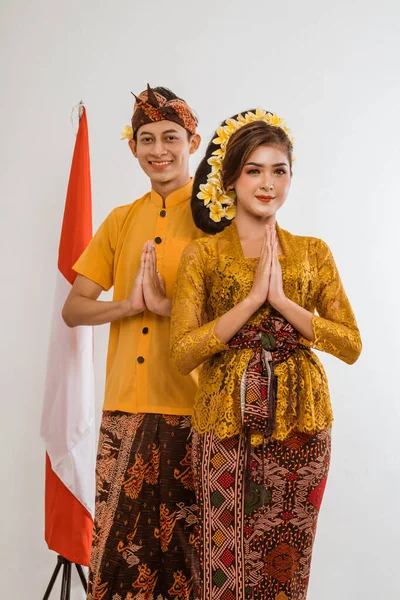 balinese couple with greeting gesture to camera. woman and man wearing traditional balinese costume over isolated background