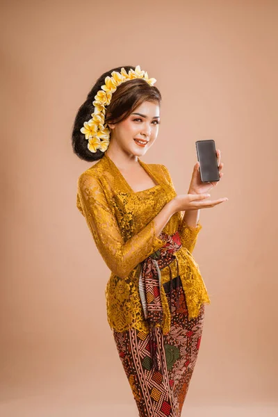 beautiful asian balinese woman with kebaya showing her mobile phone screen to camera