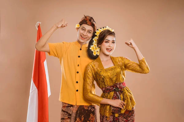 excited balinese couple put hands up looking at camera over brown background