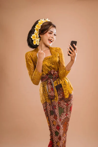 suprised balinese woman with kebaya while looking at her mobil phone screen over isolated background