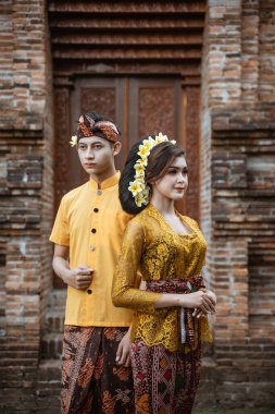 balinese couple portrait wearing kebaya dress standing in front of traditional bali gate