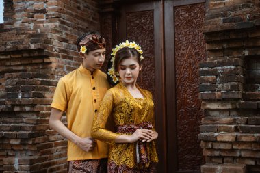 balinese couple portrait wearing kebaya dress standing in front of traditional bali gate