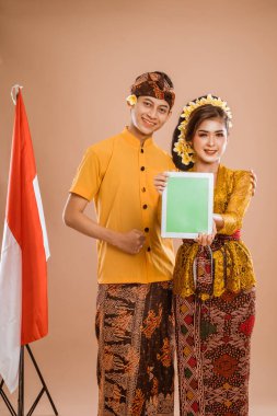 balinese young couple showing tablet screen to camera. man and woman asian wearing kebaya and traditional cloth from bali