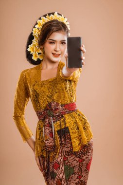 beautiful asian balinese woman with kebaya showing her mobile phone screen to camera