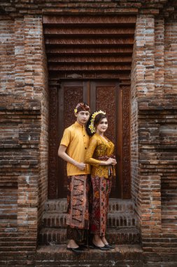 balinese couple portrait wearing kebaya dress standing in front of traditional bali gate