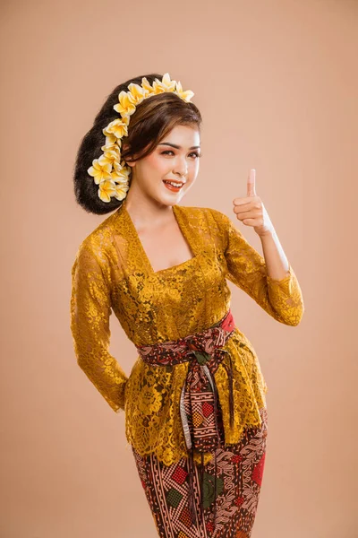 happy young balinese woman showing thumb up gesture to camera over isolated background