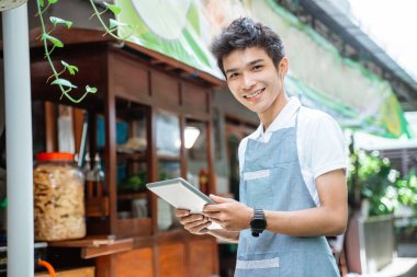 male chicken noodle seller wearing apron smiling using digital tablet on cart background