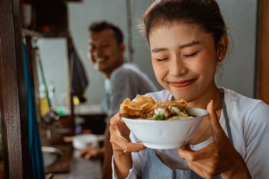 close up of female waitress smiling while bringing a bowl of delicious chicken noodles dish in a stall cart