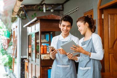 female and male sellers using tablet and mobile phone at the chicken noodle cart stall