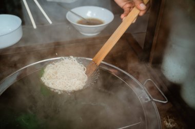 hands of seller draining boiled noodles with a sieve from the pan on the cart
