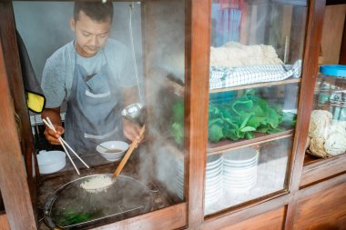 man seller pick up the cooked noodles with chopsticks from the pan on the cart