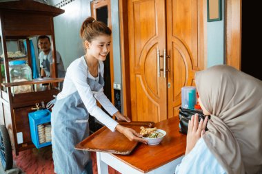 female waitress serving a bowl of delicious chicken noodles to customers in a stall cart