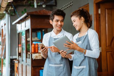 female and male sellers using pad and cellphone together at a chicken noodle cart stall