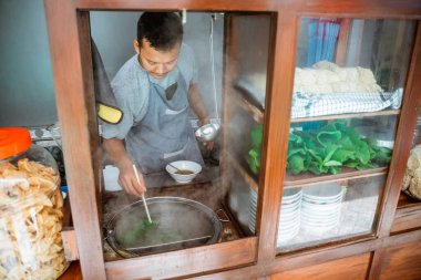 man seller boiled vegetables with chopsticks when prepare chicken noodle dish on the cart