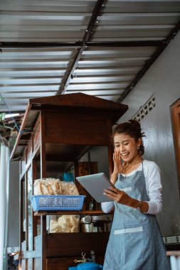 excited saleswoman in apron standing using tablet on chicken noodle cart background