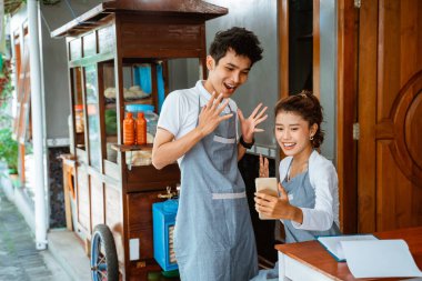 male and female sellers are surprised when using a smartphone at the chicken noodle shop