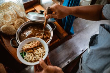 close up of sellers hand put chicken over noodles in a bowl when preparing dishes