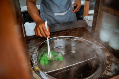 close up of mans hand boiled vegetables when prepare chicken noodle dish on the cart