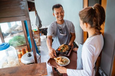 two sellers prepare a serving of chicken noodles and fried noodles on a tray