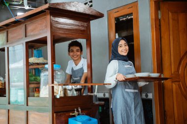 muslim sellers in apron preparing chicken noodles dish with bowls on tray for customer