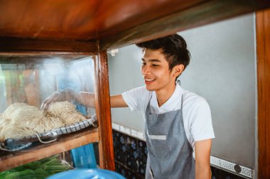 selling man wearing an apron takes noodles while cooking in a chicken noodle cart