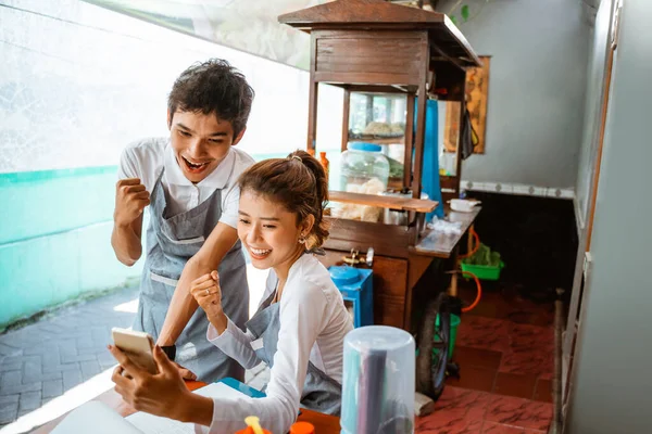 male and female sellers are happy to see cellphones with clenched fists at a chicken noodle shop