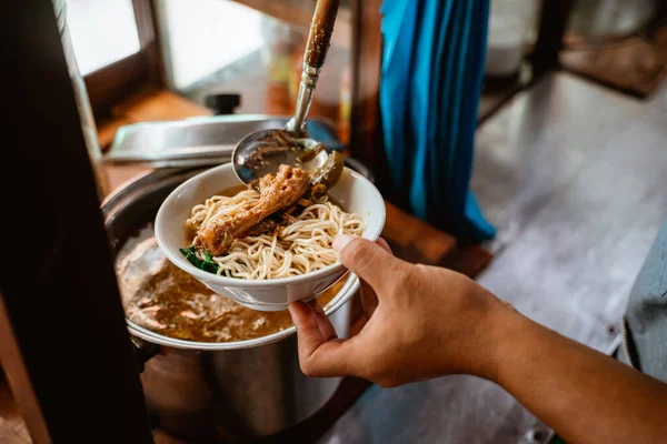 close up of sellers hand put chicken on noodles in a bowl for topping when preparing dishes