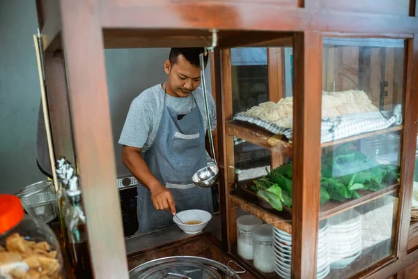 man seller in apron stir the spices in the bowl when preparing chicken noodles dish