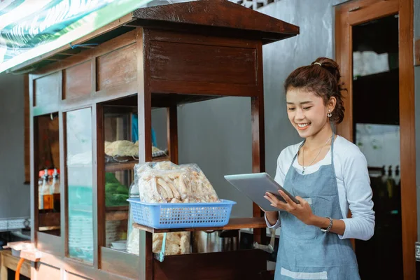 saleswoman wearing apron standing using digital tablet with chicken noodle cart background