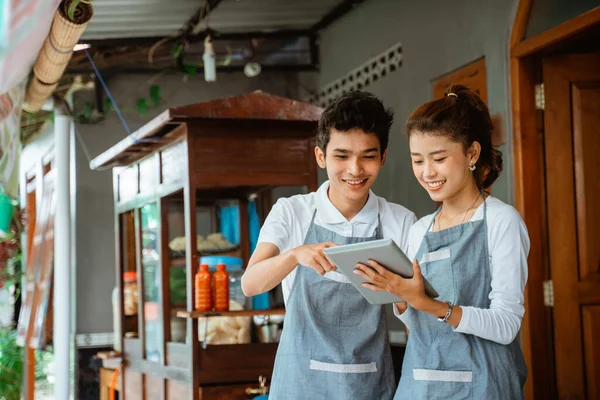 smiling woman and man merchant using digital tablet at chicken noodle cart stall