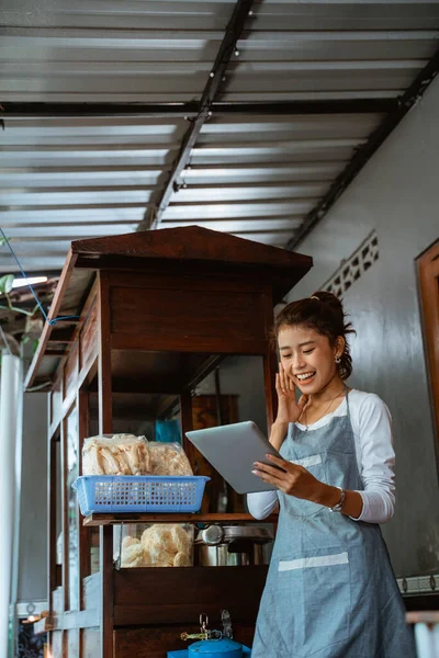 excited saleswoman in apron standing using tablet on chicken noodle cart background