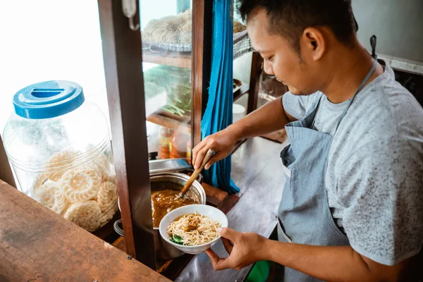 man seller giving chicken to noodles when preparing dishes on the cart