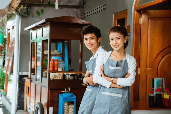 female and male traders smiling with arms crossed at a chicken noodle cart stall