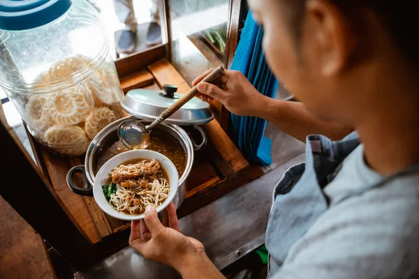 man seller put chicken topping over noodles in a bowl when preparing dishes